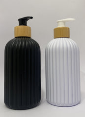Two ribbed pump bottles on a light gray background, one black with a bamboo-look gold cap and black pump, and one white with a bamboo-look gold cap and white pump.