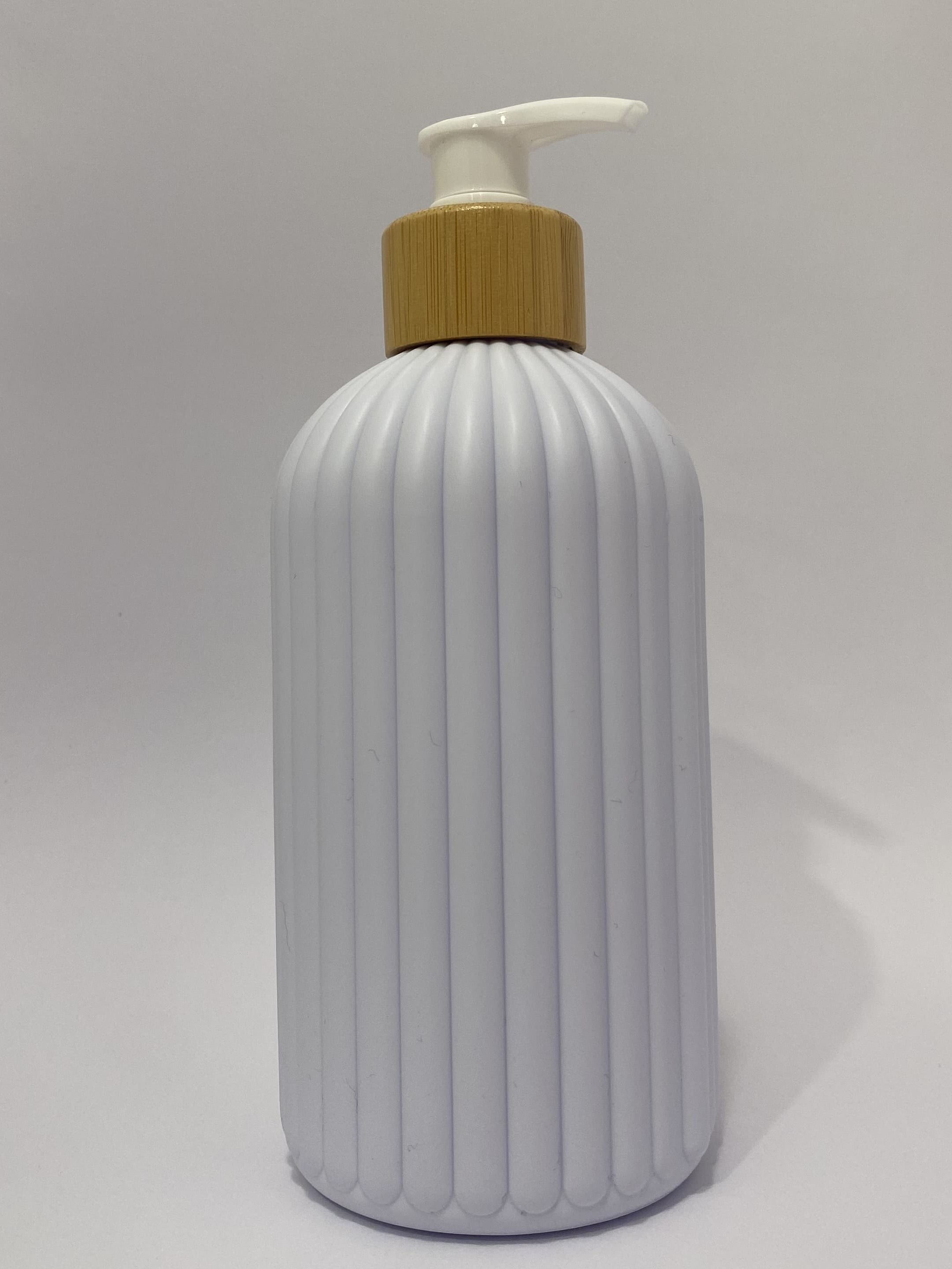 A ribbed white plastic bottle with a gold-colored collar and a white pump dispenser, shown against a plain white background.